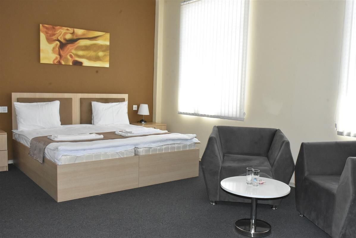 Een hotelkamer met een bed, twee nachtkastjes, een klein rond tafeltje met twee glazen en twee fauteuils.