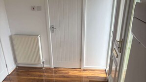 Et værelse med trægulv, en hvid dør, en radiator og en trappe.