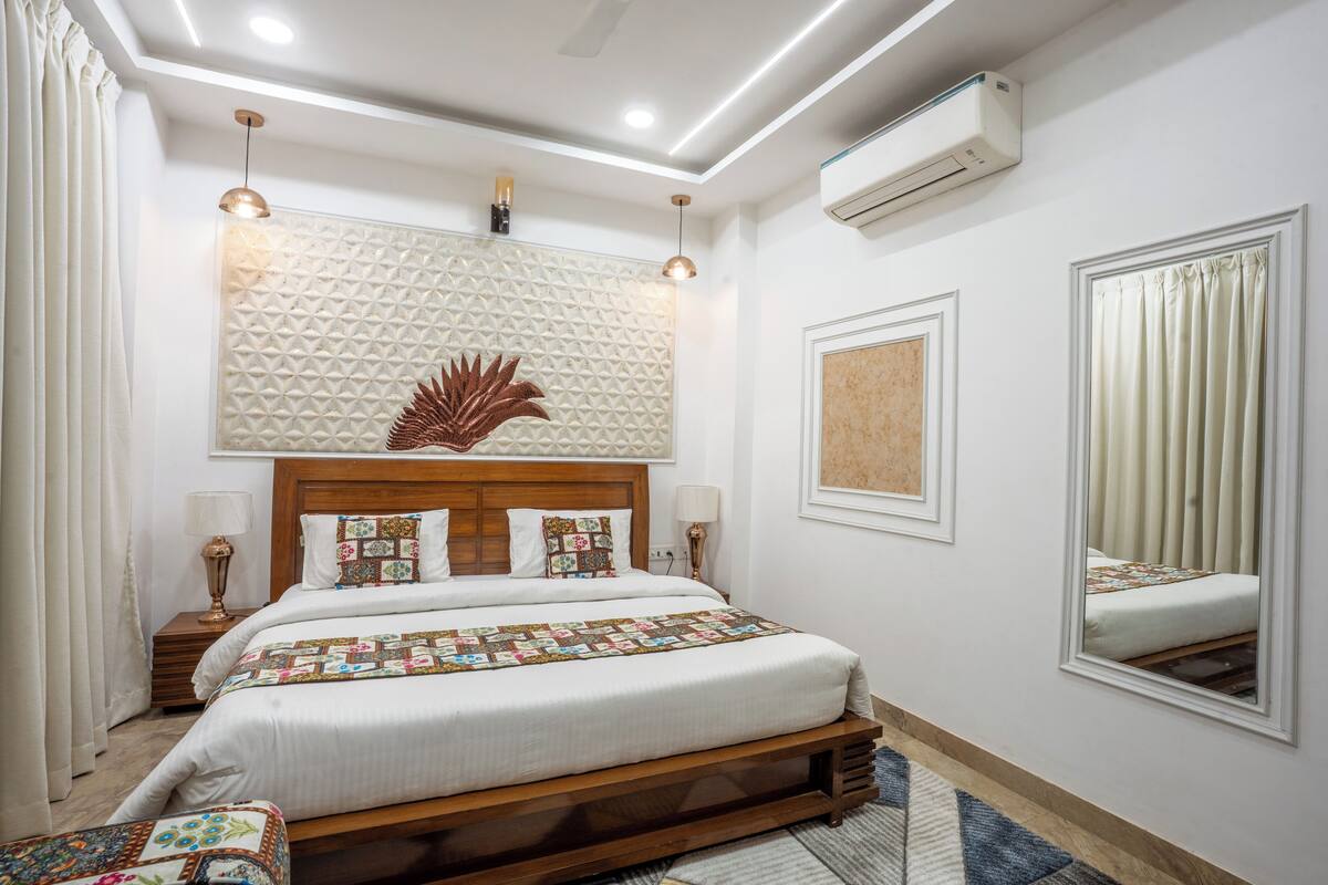 Une chambre moderne avec un grand lit, un panneau décoratif au mur, un luminaire au plafond, un appareil de climatisation et un miroir.