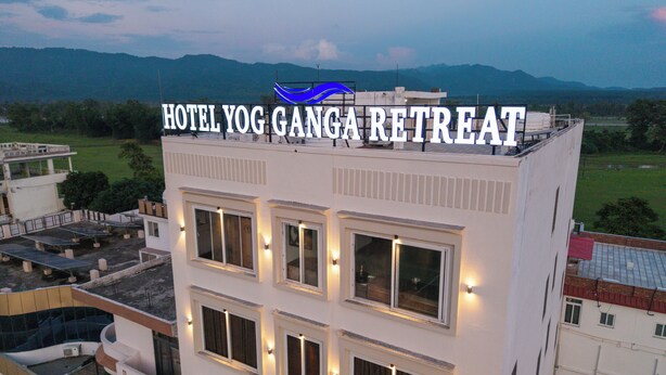 Un hotel llamado "Hotel Yog Ganga Retreat" con múltiples ventanas y vistas del paisaje circundante.