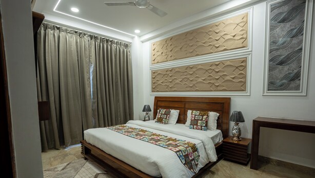 Ein Schlafzimmer mit einem großen Bett, einem hölzernen Kopfteil, zwei Nachttischen mit Lampen, einem Beistelltisch, einer Holzbank, einem gemusterten Teppich und einem Deckenventilator.