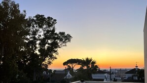 En tagterrasse med udsigt over solnedgang, træer og fjerne bygninger.