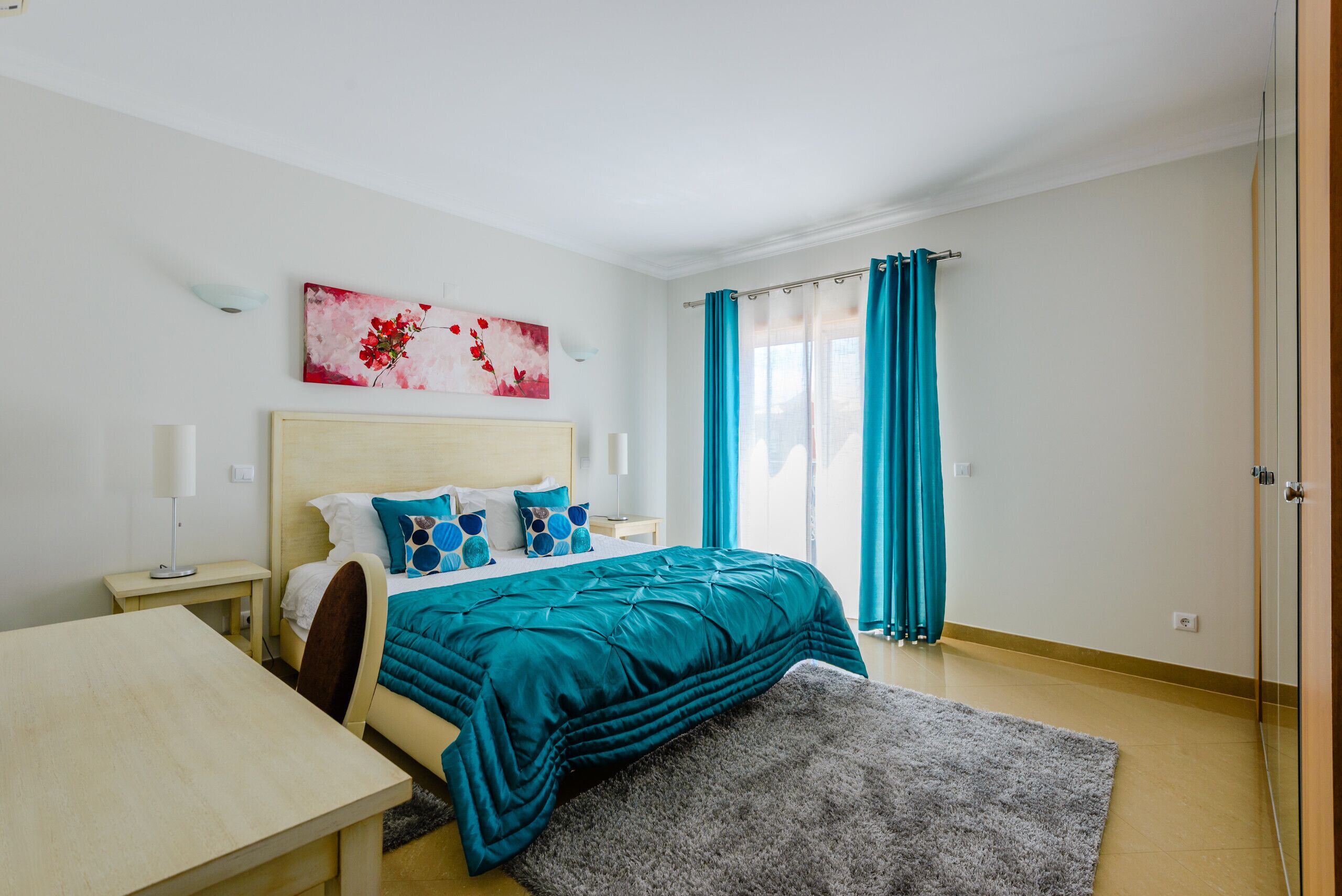 Une chambre à coucher avec un lit, des tables de chevet, un bureau, un tapis et un tableau au mur.