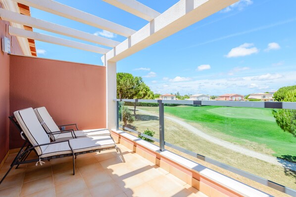 A balcony with two lounge chairs, a view of a green landscape, and a clear sky.