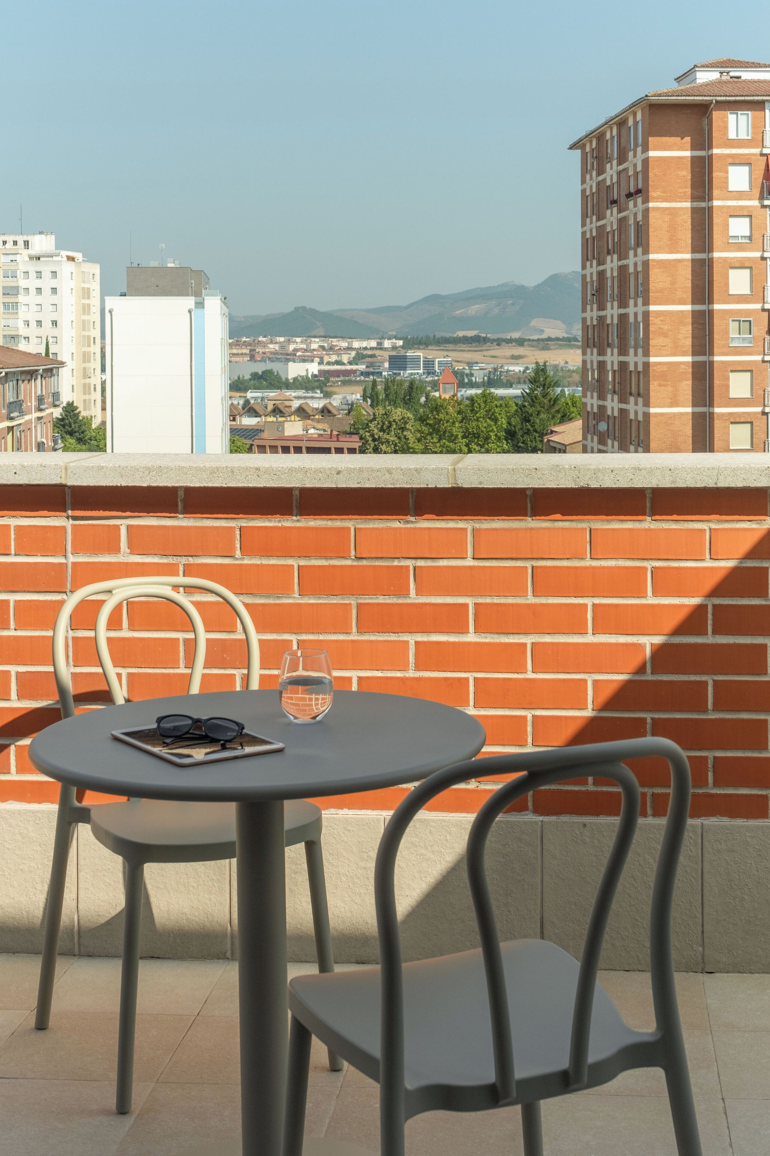 Un balcón con una mesa redonda y dos sillas, un vaso de agua y un par de gafas sobre la mesa.
