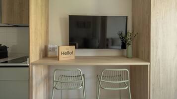 A modern kitchen with a wooden countertop, a flat-screen TV mounted above, and two green metal chairs.