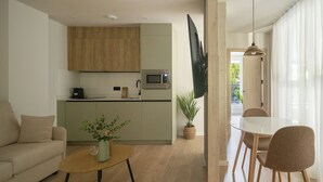 A modern living room with a sofa, a coffee table with a plant, a dining area with a table and chairs, a kitchen with wooden cabinets and a microwave, and a large TV mounted on the wall. - Líbere Pamplona Universidad (Pamplona)