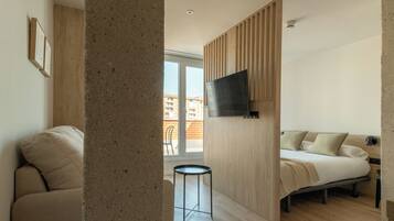 Een moderne hotelkamer met een bed, een aan de muur bevestigde televisie, een klein tafeltje en uitzicht op het balkon.