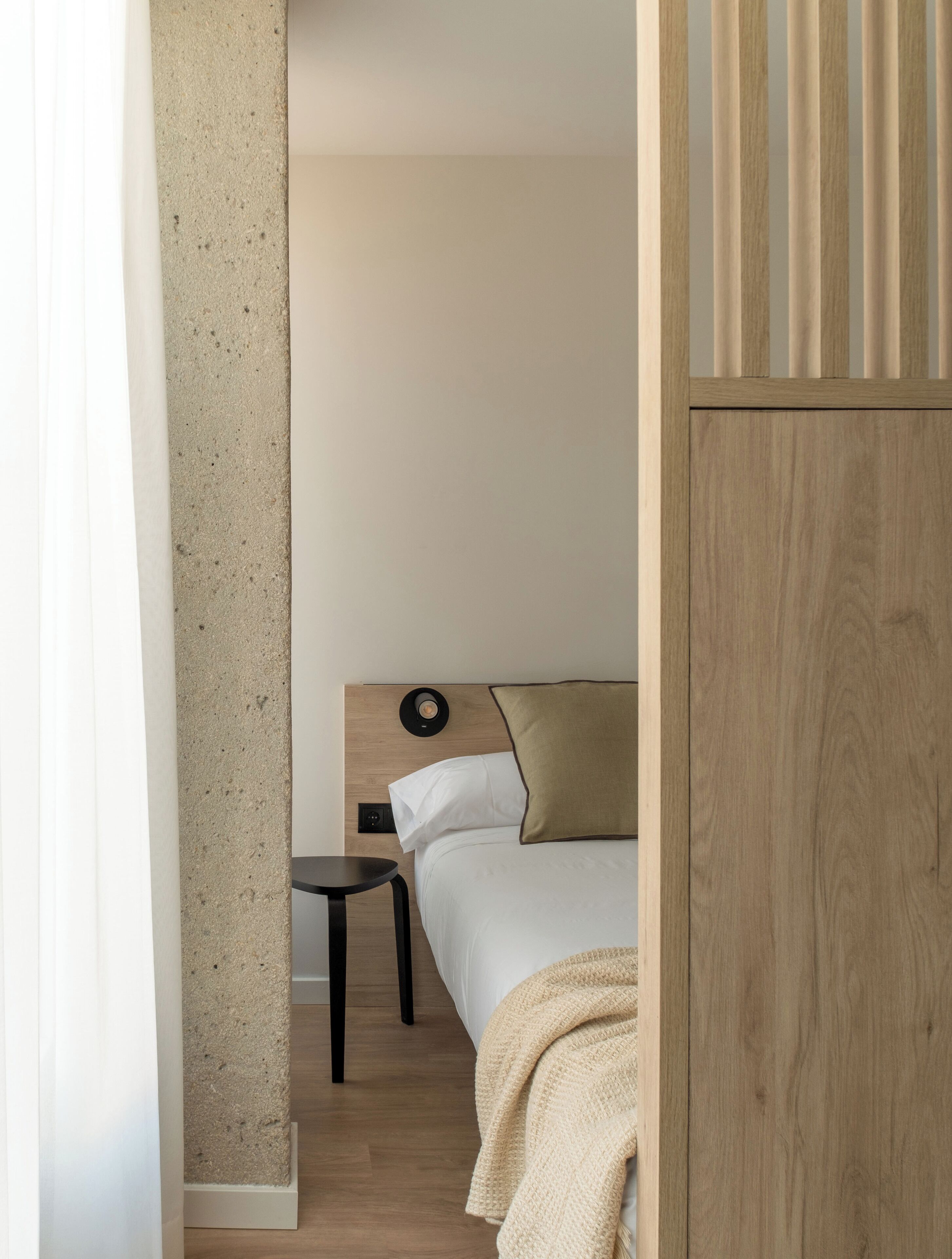 Un dormitorio con cama, mesita de noche, luz empotrada en la pared y cabecero de madera.