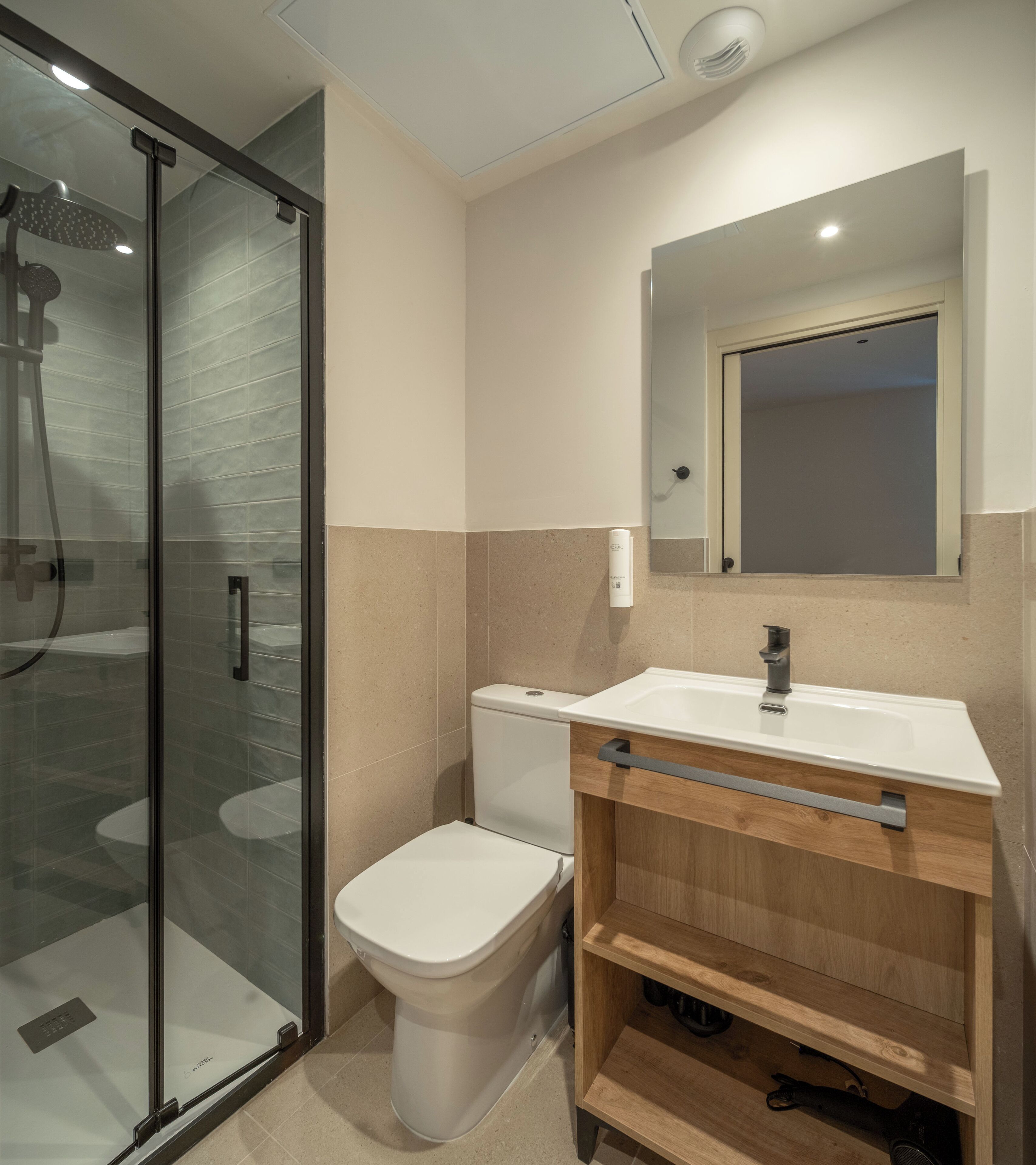 Un baño moderno con cabina de ducha de vidrio, inodoro, lavabo con espejo y tocador de madera.