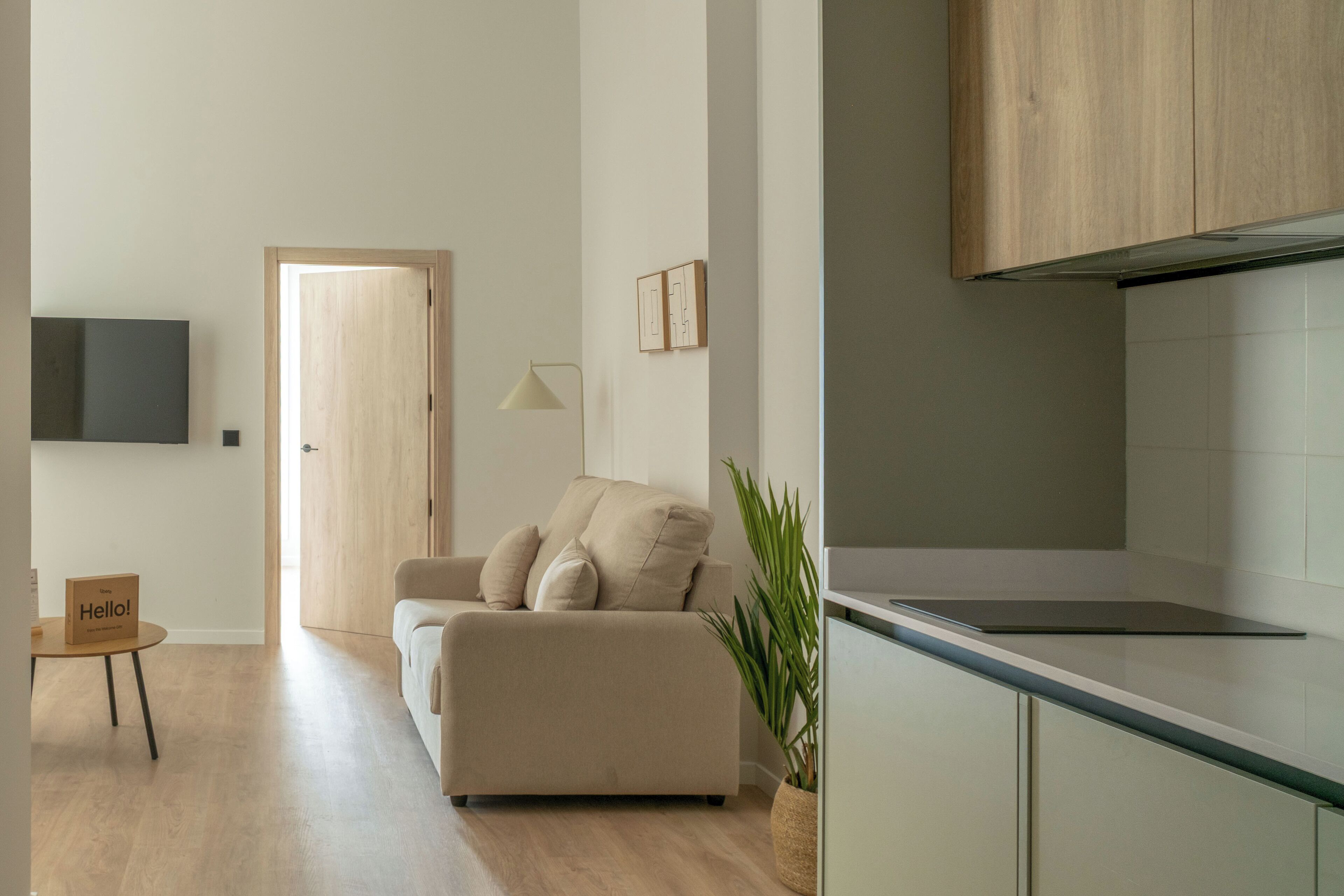 Una sala de estar moderna con un sofá, un televisor montado en la pared, una puerta de madera y una mesita con un letrero.