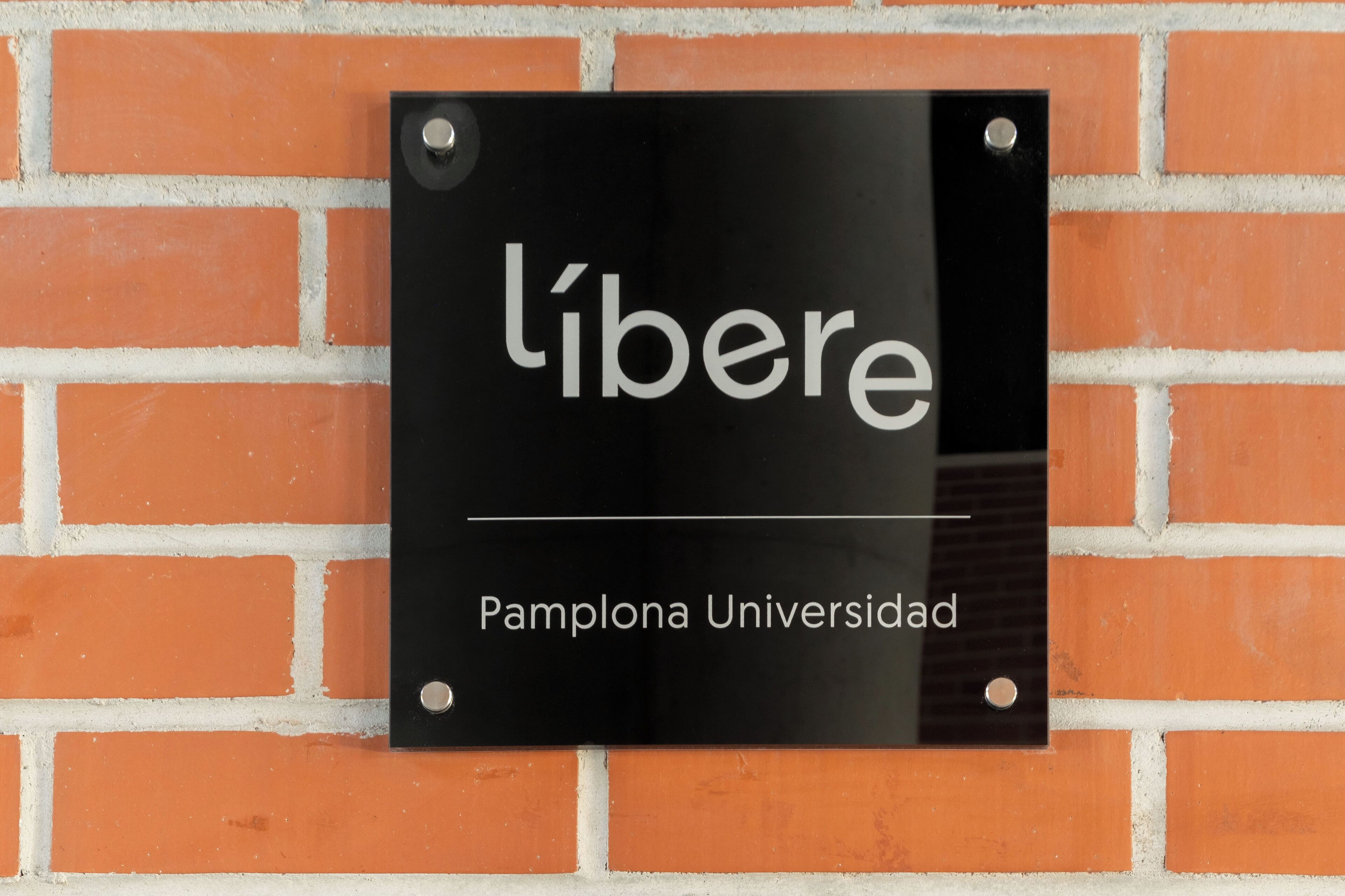 Et sort skilt med hvid tekst, der viser "l'iberé Pamplona Universidad", monteret på en murstensmur.