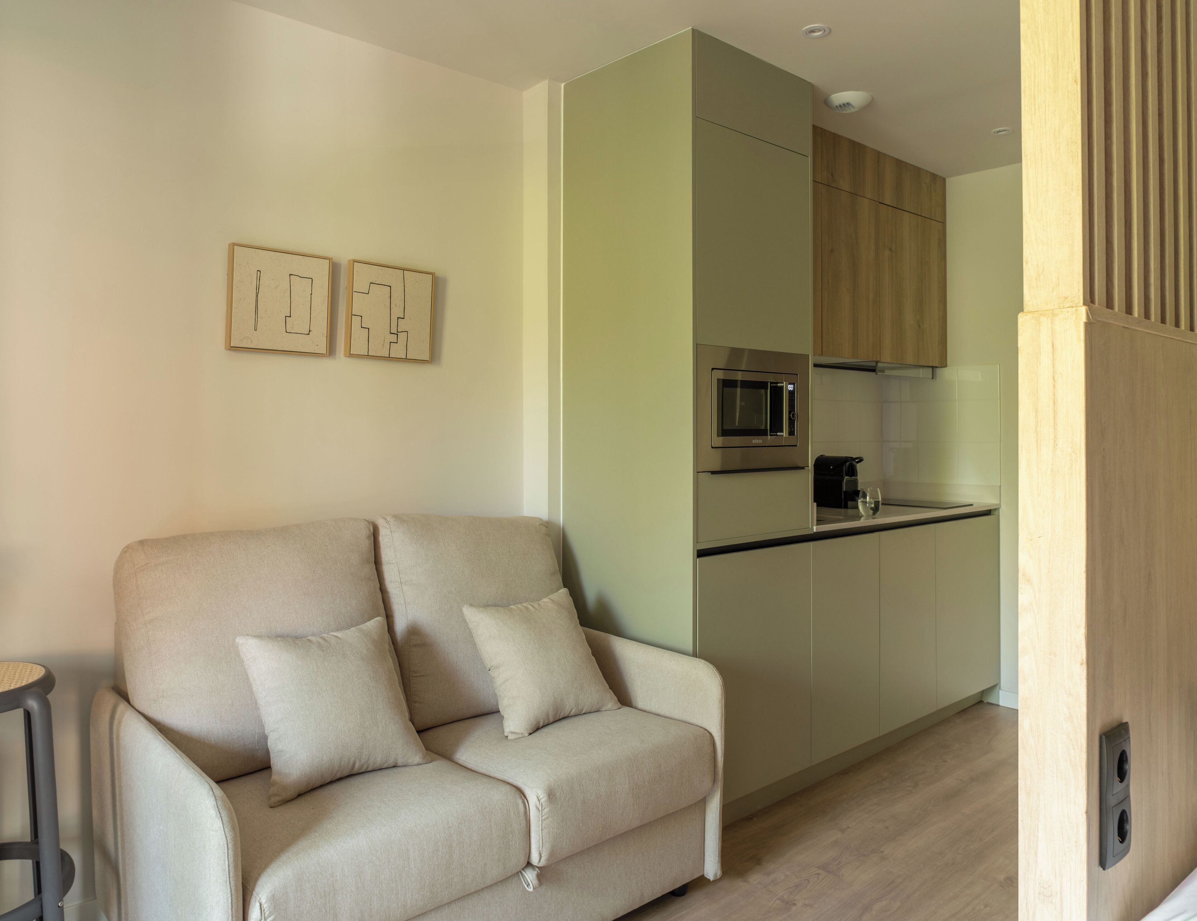 A modern living room with a sofa and a kitchen area featuring a microwave and a coffee maker.