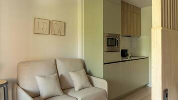 A modern living room with a sofa and a kitchen area featuring a microwave and a coffee maker.