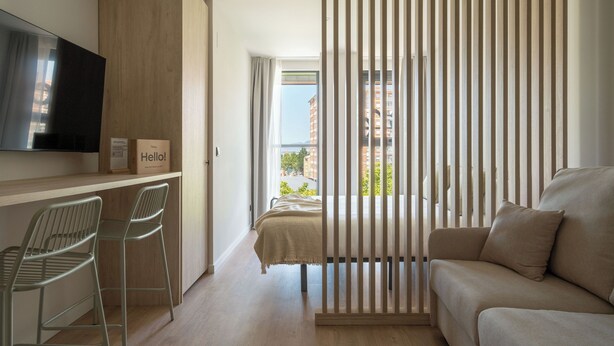 A modern hotel room with a bed, a sofa, a TV, and a desk with two chairs. - Líbere Pamplona Universidad (Pamplona)