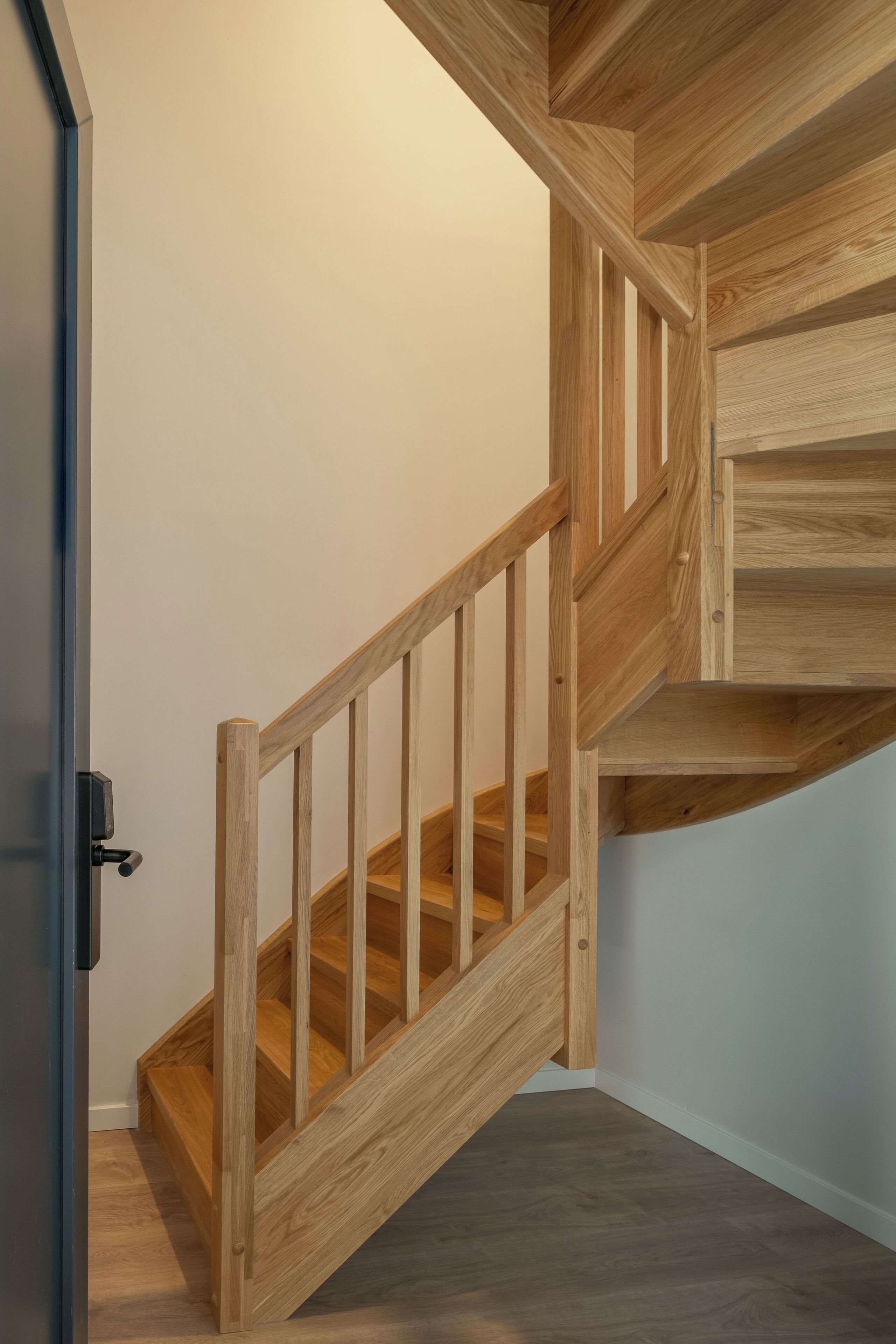 Un escalier en bois, avec une rampe et une porte sur le côté gauche.