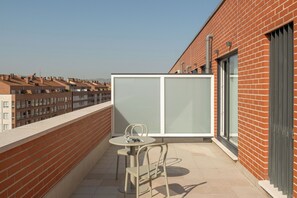 A balcony with a table and chairs, a glass partition, and a view of neighboring buildings. - Líbere Pamplona Universidad (Pamplona)
