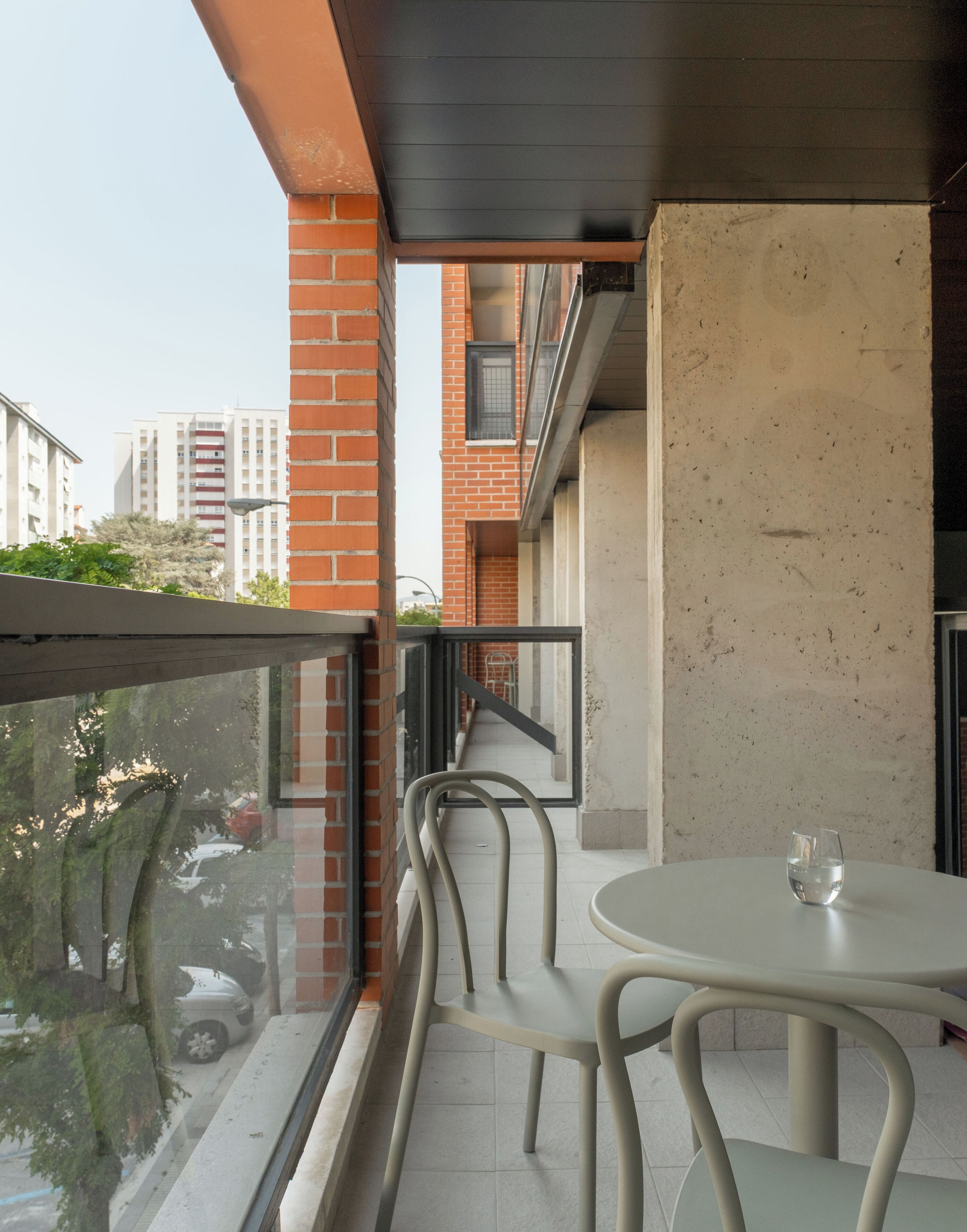 A balcony with a table and chairs, a glass railing, and a view of a cityscape.