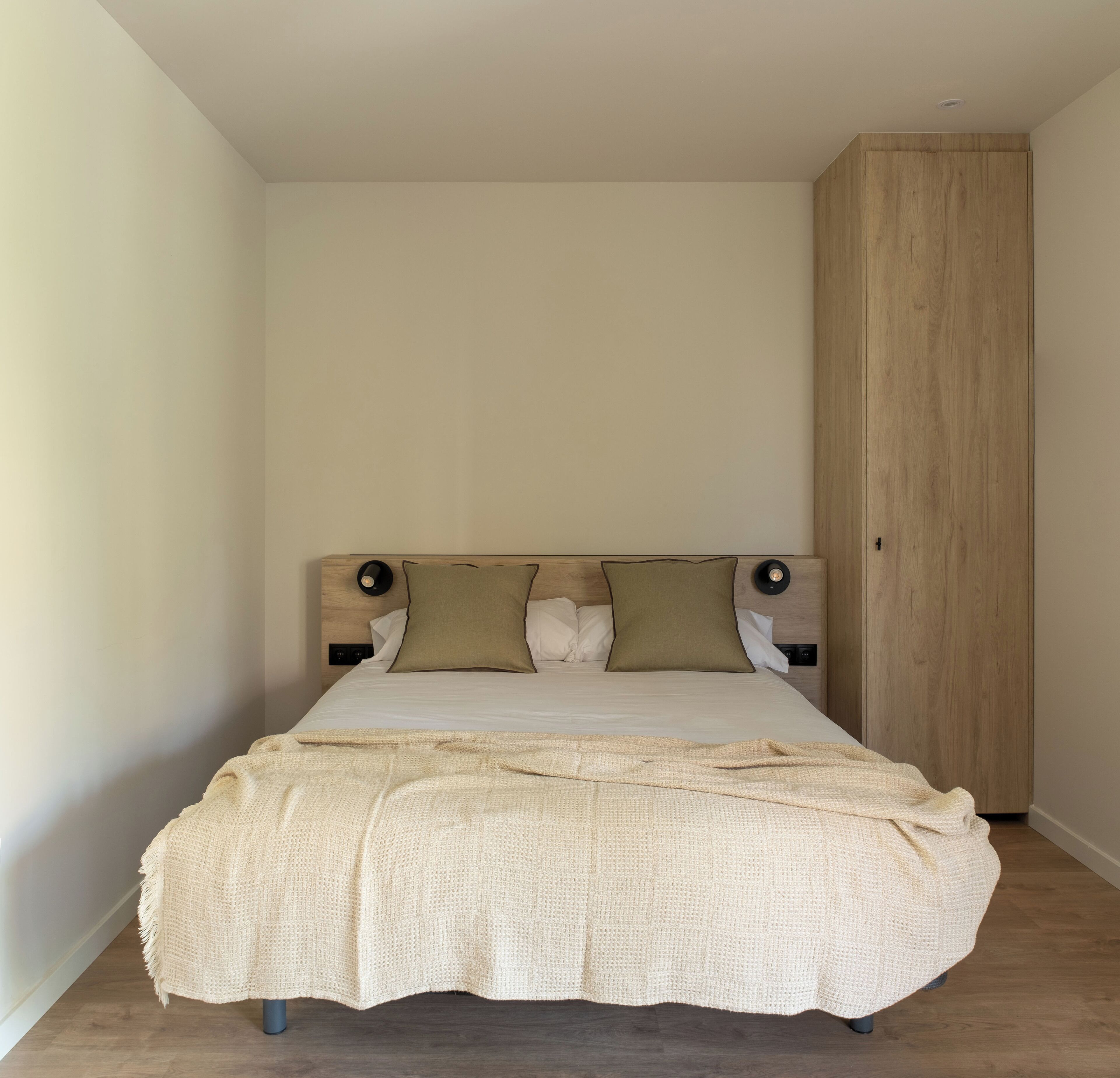 A bedroom with a bed, a wooden wardrobe, and a nightstand with a lamp.