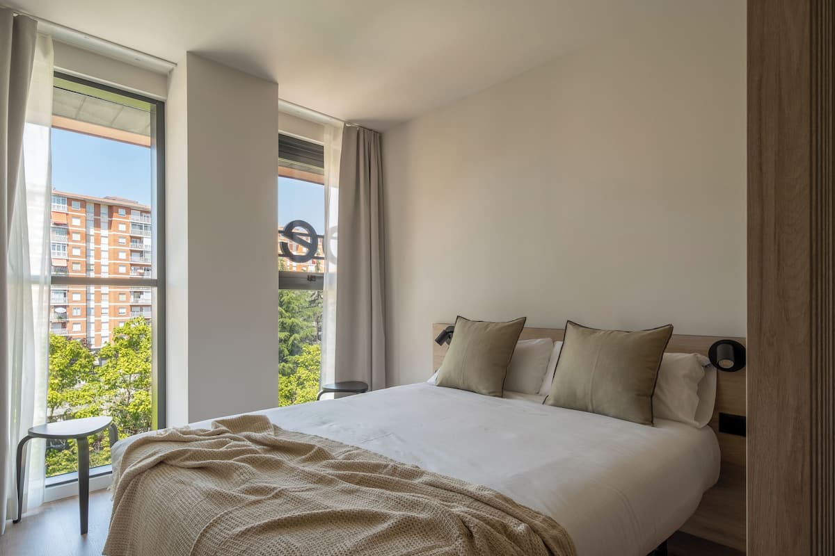 A modern hotel room with a large bed, a view of the city, and a balcony.