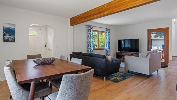 A modern living room with a wooden ceiling, a dining table with chairs, a sofa, a TV, and a window with curtains. - Quintessential University District Home (Missoula)