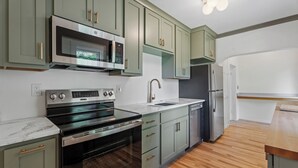 A modern kitchen with green cabinets, stainless steel appliances, and a wooden floor. - Quintessential University District Home (Missoula)