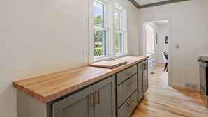 A kitchen with a wooden countertop, grey cabinets, and a window with a view of greenery. - Quintessential University District Home (Missoula)