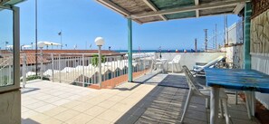 Un espace extérieur abrité, doté d’un sol carrelé, de chaises blanches, d’une table et offrant une vue sur la mer.