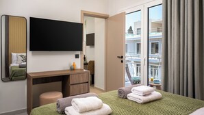 A hotel room with a bed, a desk, a flat-screen TV, a mirror, and a balcony with a view of the building.