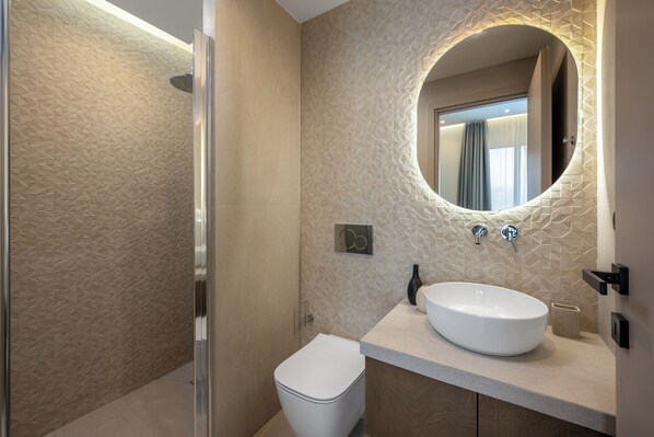 A modern bathroom with a large oval sink, a toilet, and a shower area.