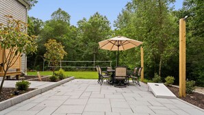 Une terrasse avec une table et des chaises, entourée d’un jardin et d’arbres.