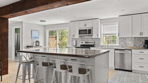 Une cuisine moderne avec des meubles blancs, un grand îlot central doté de tabourets, un four à micro-ondes et un lave-vaisselle.