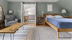Une chambre à coucher comprenant un lit, des tables de chevet, une chaise, une table en bois et un miroir.