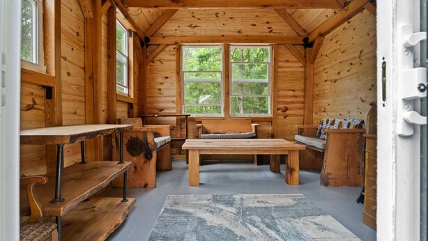 L’intérieur d’un chalet en bois, avec une grande fenêtre, une table centrale, des bancs et un tapis à motifs.