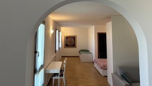 A hallway leading to a dining area with a table and chairs, a bed with a patterned bedspread, and a framed artwork on the wall.