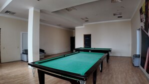 A room with two pool tables, wooden flooring, and a door leading to another room.