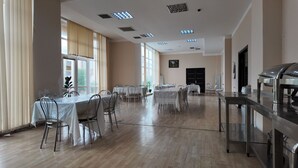 A spacious dining hall with multiple tables and chairs, large windows, and ceiling lights.