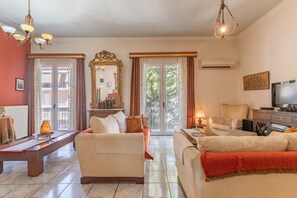 Una sala de estar con un sofá, una mesa de centro y un televisor. Hay un espejo grande y una ventana con cortinas.