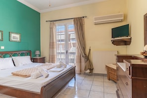Una habitación de hotel con cama, cómoda de madera, televisor y ventana con cortinas.