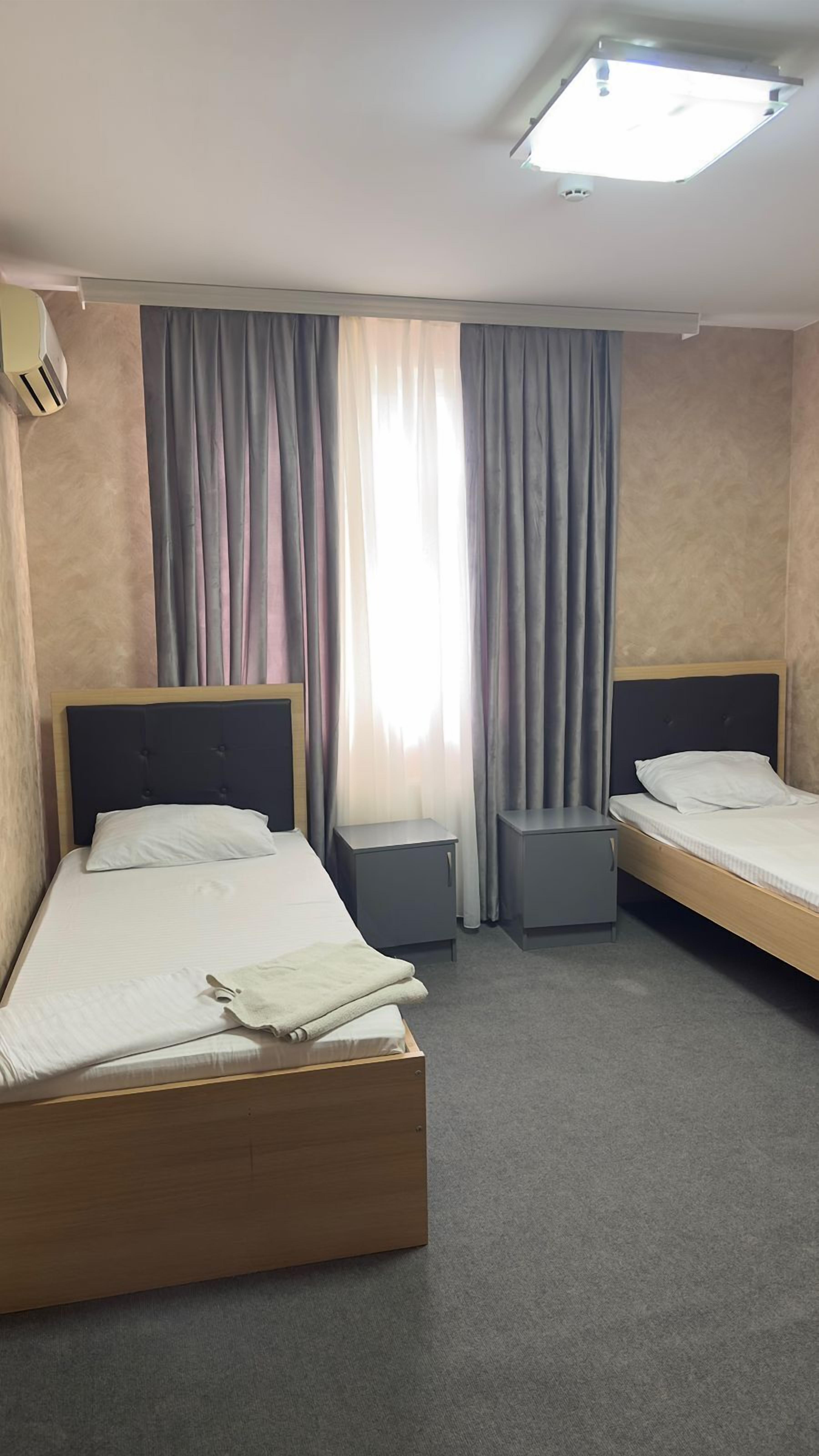 Une chambre d’hôtel avec deux lits simples, une petite table de chevet, une commode et un appareil de climatisation fixé au plafond.