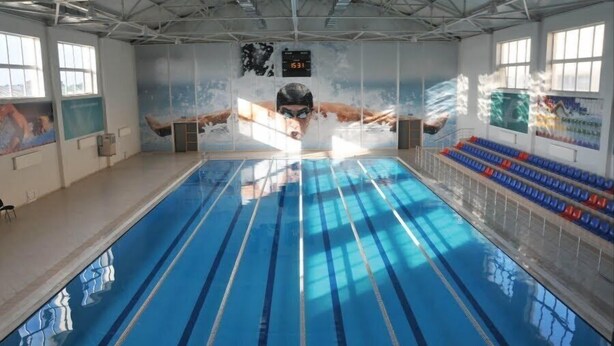An indoor swimming pool with lanes, a digital clock, and a mural on the wall. - Arena Hotel Shagan (Baku)