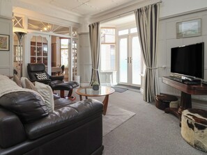 A living room with a leather sofa, a black armchair, a glass coffee table, a television, and a cowhide ottoman. - Sandy Shore (Bridlington)