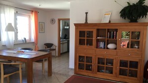 Ein Essbereich mit einem Holztisch und Stühlen, im Hintergrund eine Küche und ein Holzschrank mit Glastüren.