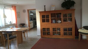 Ein Essbereich mit Holztisch und Stühlen, im Hintergrund eine Küche und ein großer Schrank mit Glastüren.