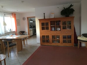 Ein Essbereich mit Holztisch und Stühlen, im Hintergrund eine Küche und ein großer Schrank mit Glastüren.