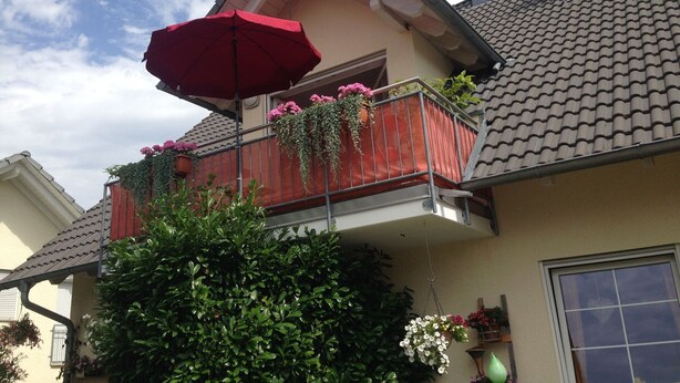 Ein Wohngebäude mit Balkon, einem roten Sonnenschirm und Blumentöpfen.