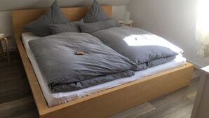 Ein Bett mit Holzrahmen, grauer Bettwäsche und zwei Kissen.