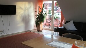Ein Wohnzimmer mit einer Couch, einem Tisch, einer Topfpflanze und einer Glastür zum Außenbereich.