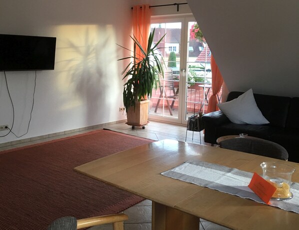 A living room with a sofa, a table, a potted plant, and a sliding glass door leading to an outdoor area.