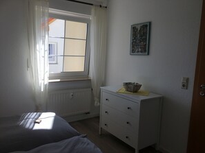 A bedroom with a bed, a dresser, a radiator, a window with curtains, and a painting on the wall.